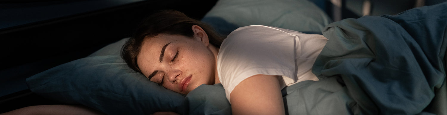Woman sleeping peacefully in bed with blue pillows and a white blanket.